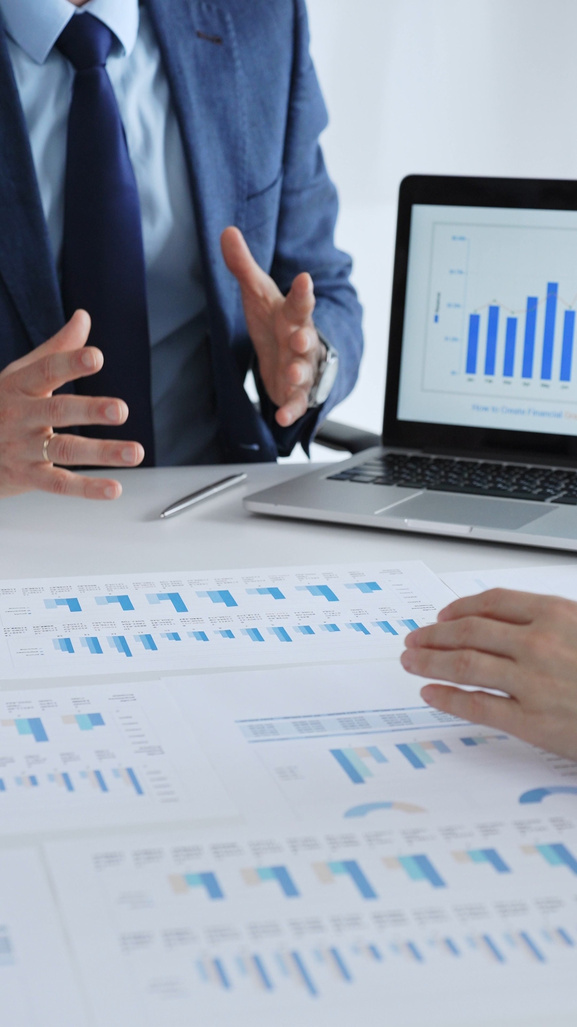 Business people collaborating at a table, discussing financial data and reports with a calculator and laptop displaying charts, focusing on strategy and planning, close up vertical view